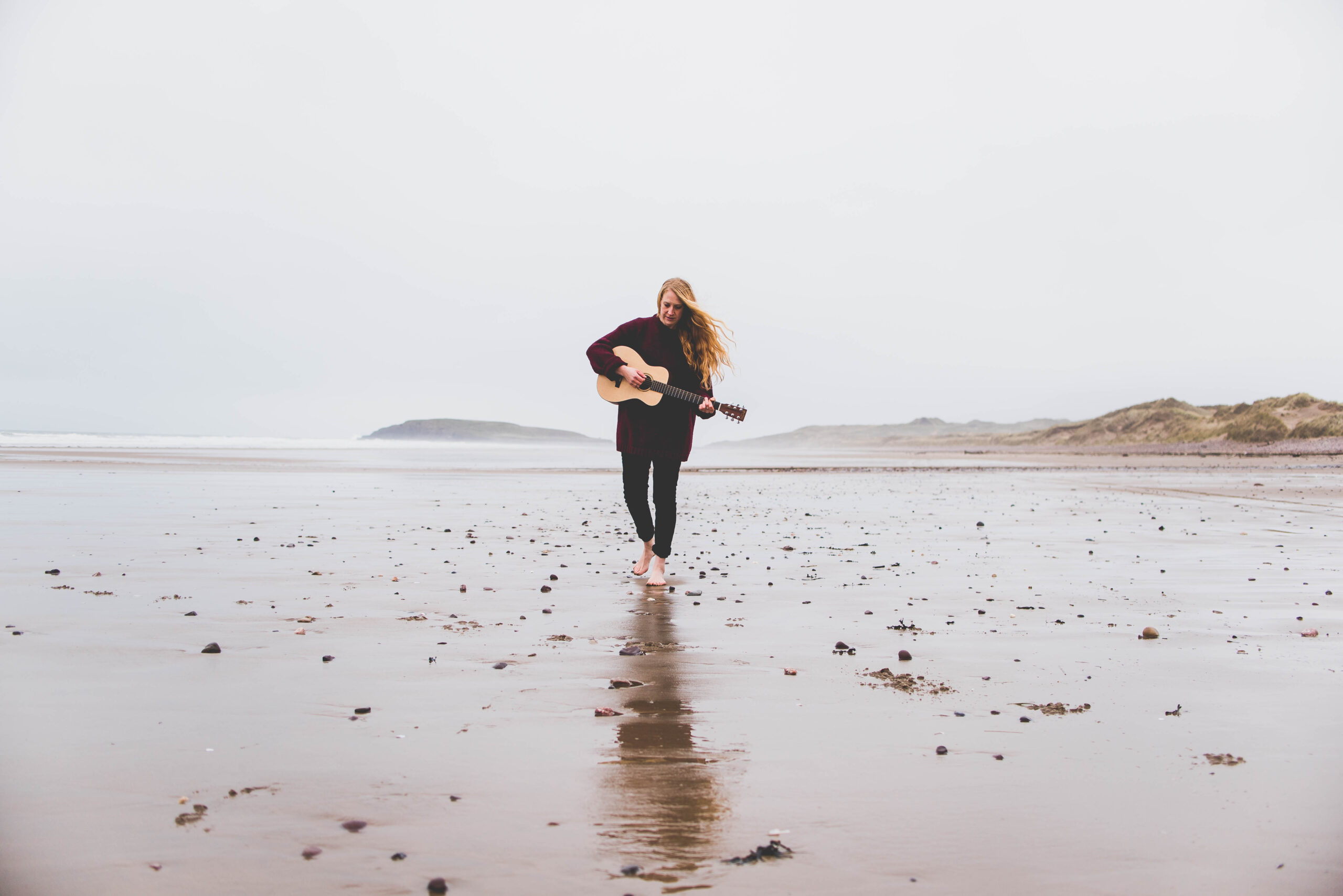 Eleanor walking on the beach playing her guitar